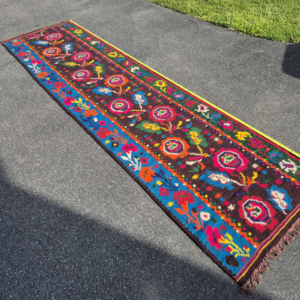 Full high-angle shot of a stunning 11-foot vintage Caucasian floral Kilim runner rug laid out on asphalt, displaying vivid pink, orange, and blue medallions over a black background