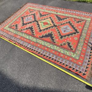 Full high-angle shot of a vintage 5'x7' Balkan tribal Kilim rug on asphalt, showcasing three large stepped diamond medallions on a terracotta ground with a tape measure layout.