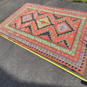 Full high-angle shot of a vintage 5'x7' Balkan tribal Kilim rug on asphalt, showcasing three large stepped diamond medallions on a terracotta ground with a tape measure layout.
